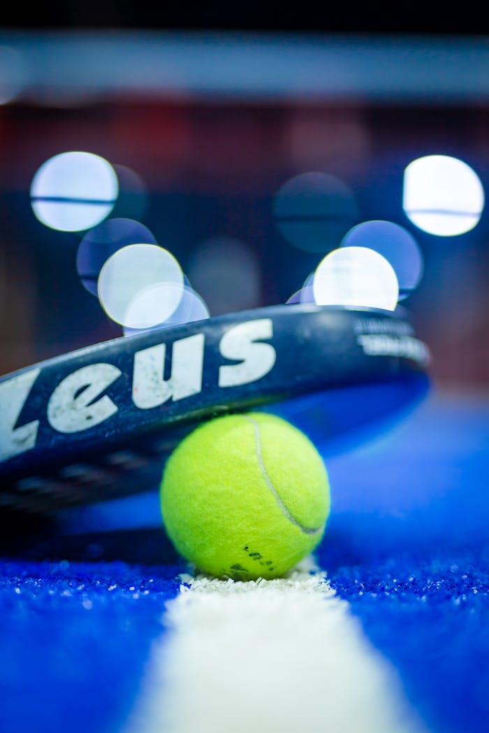 Vibrant image of a padel racket and yellow ball on a blue court, highlighting sports equipment.