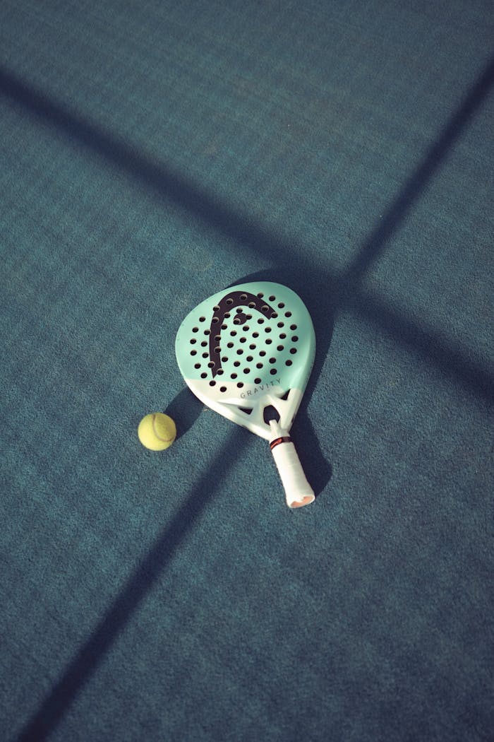 Close-up of a padel racket and ball on a sunlit court, emphasizing the sport's dynamic nature.